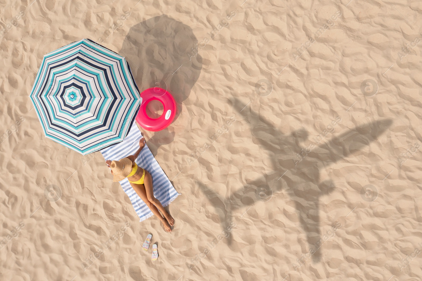 Woman resting under striped umbrella on beach, top view. Flying airplane casting shadow on sand Image of Woman resting under striped umbrella on beach, top view. Flying airplane casting shadow on sand