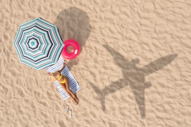 Image of Woman resting under striped umbrella on beach, top view. Flying airplane casting shadow on sand