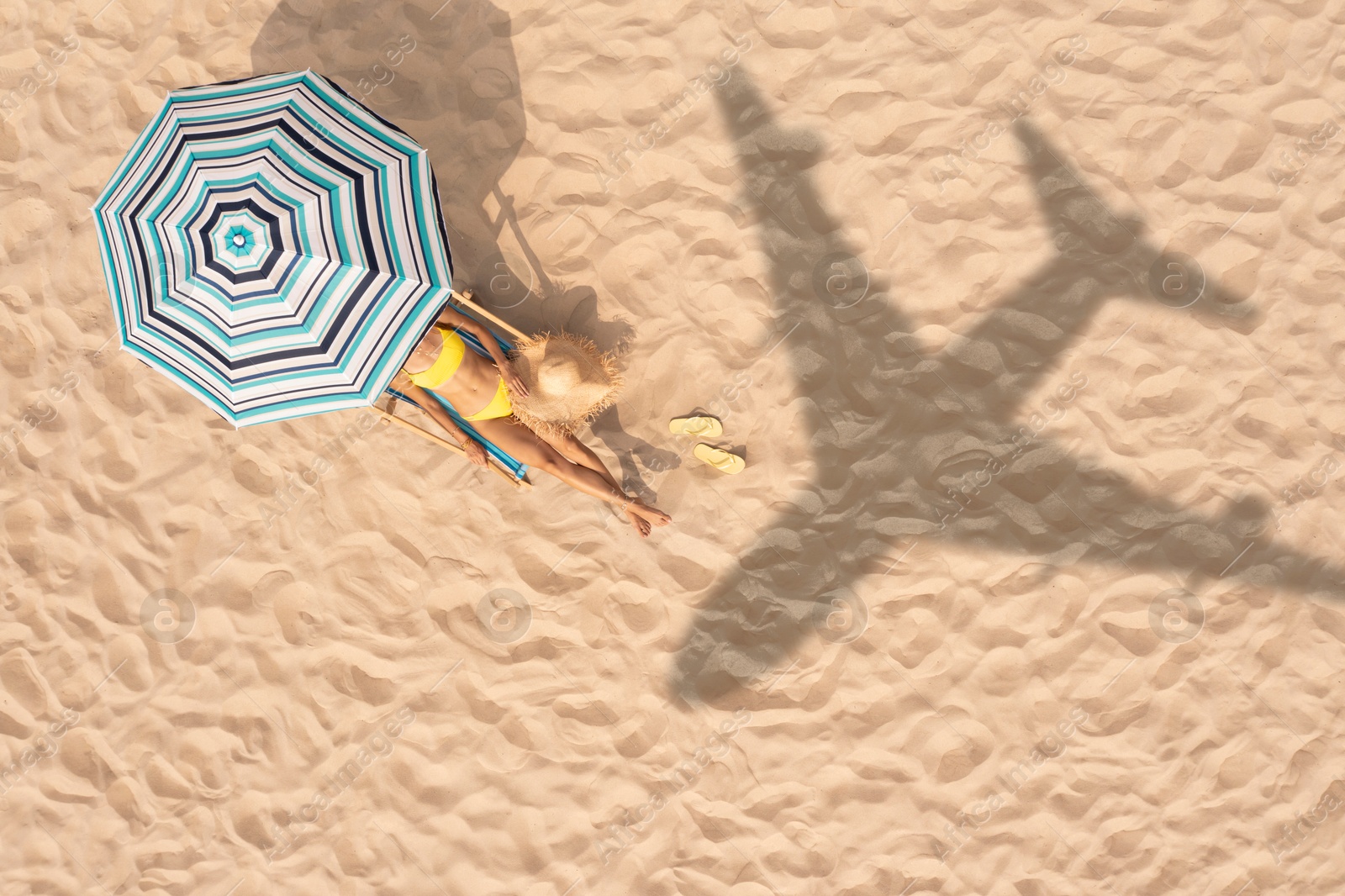 Woman resting under striped umbrella on beach, top view. Flying airplane casting shadow on sand Image of Woman resting under striped umbrella on beach, top view. Flying airplane casting shadow on sand