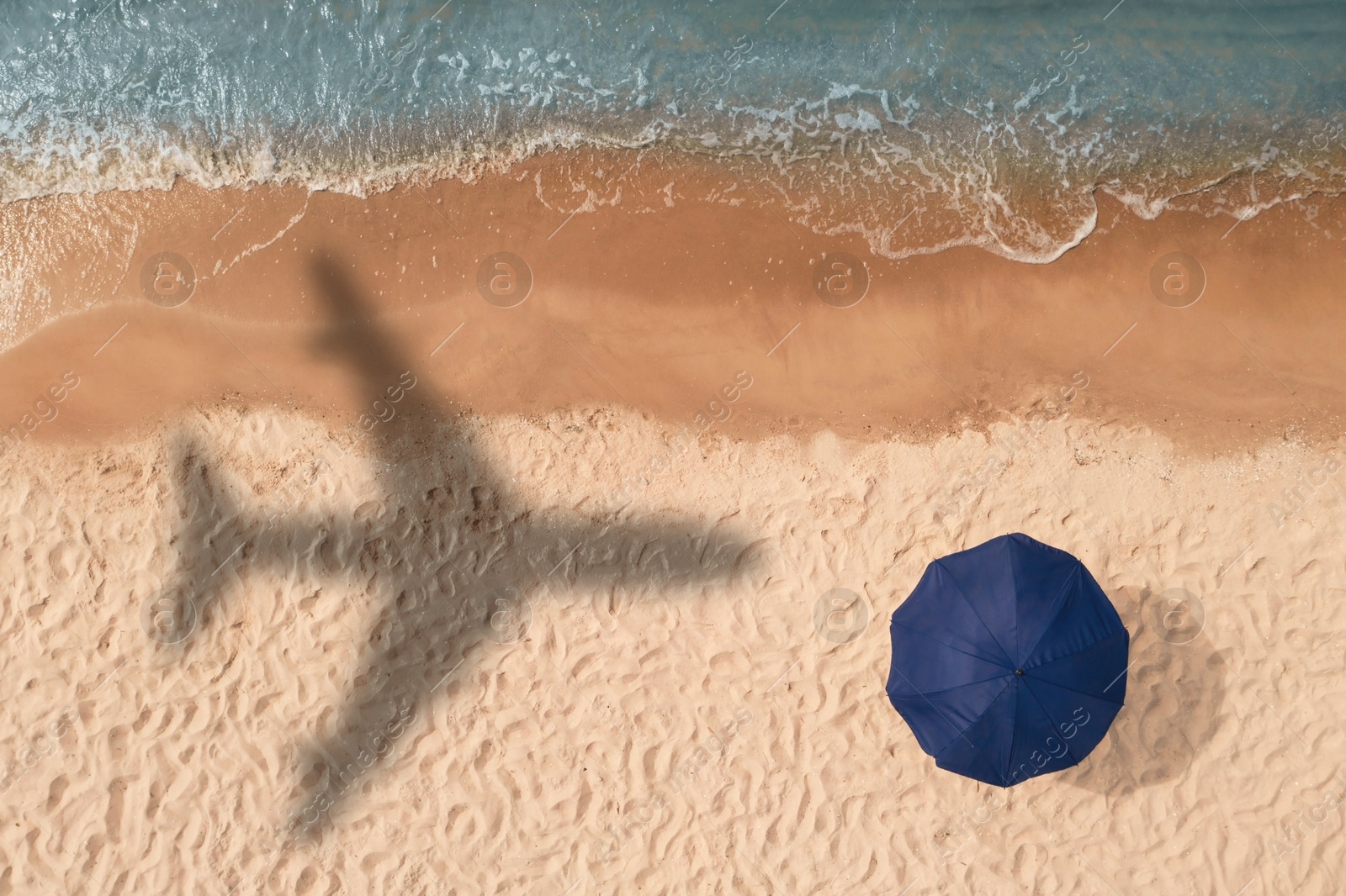 Flying airplane casting shadow on sand with beach umbrella, top view Image of Flying airplane casting shadow on sand with beach umbrella, top view