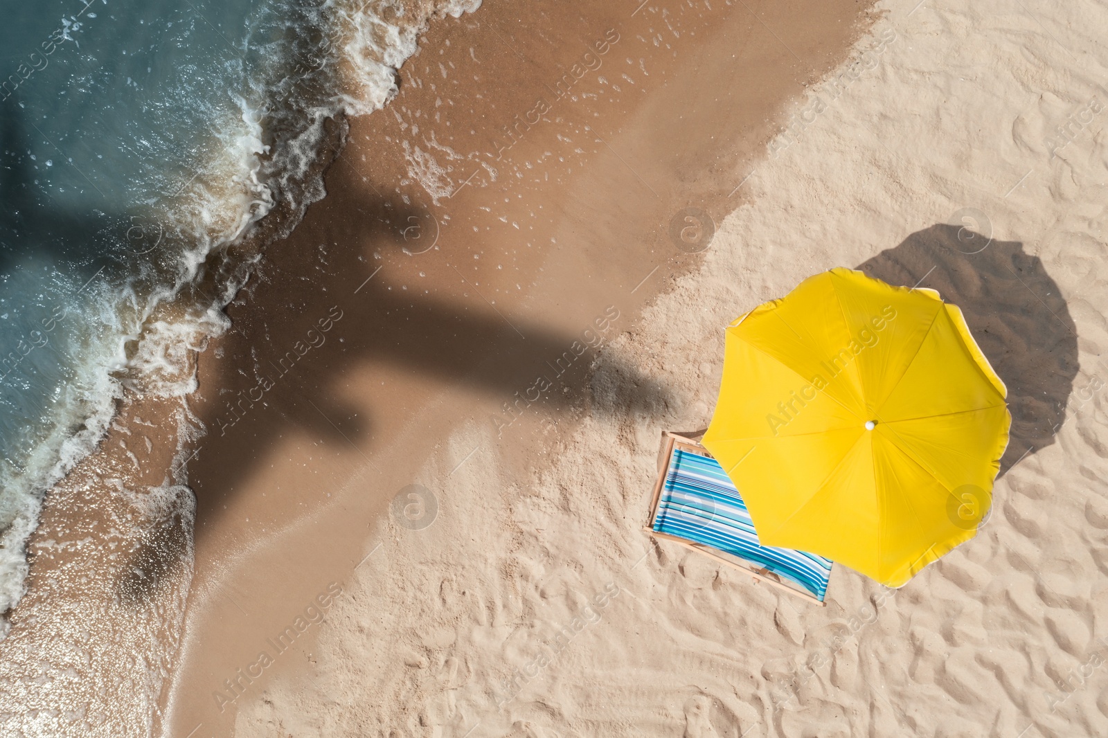 Yellow umbrella and deck chair on beach, top view. Flying airplane casting shadow on sand and water Image of Yellow umbrella and deck chair on beach, top view. Flying airplane casting shadow on sand and water