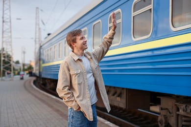 Photo of Goodbye. Happy man waving near train outdoors