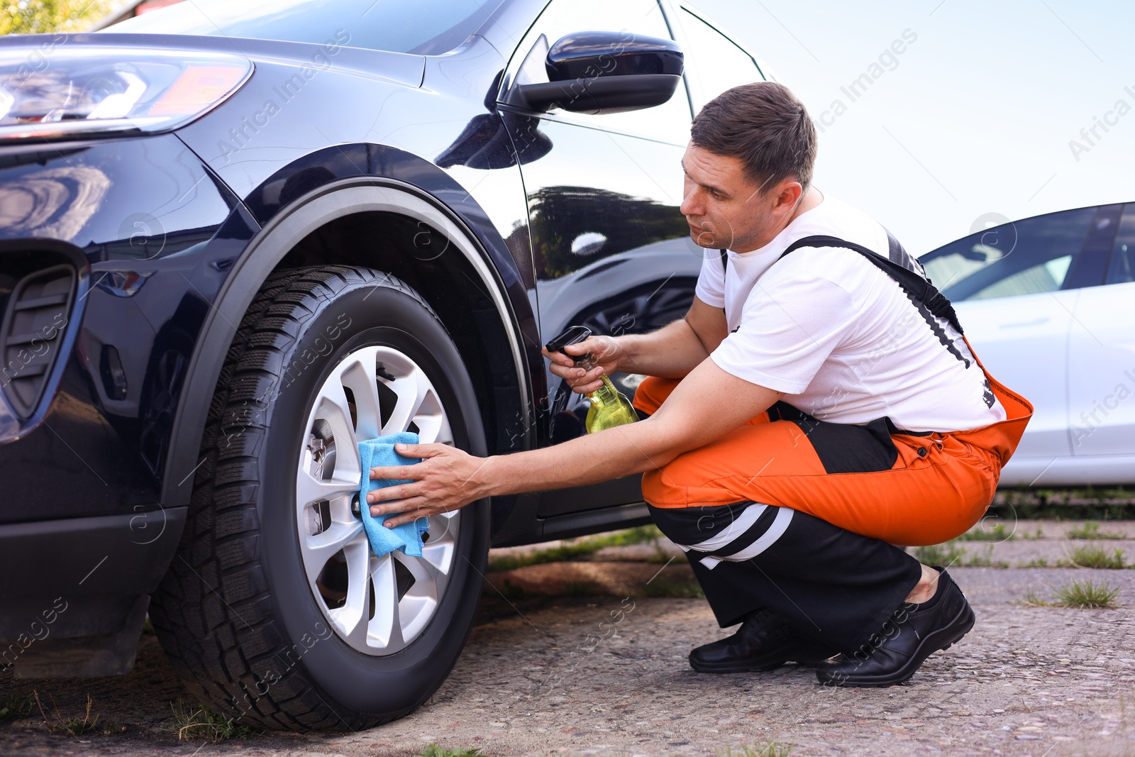 Man wiping car wheel with blue microfiber rag outdoors Photo of Man wiping car wheel with blue microfiber rag outdoors
