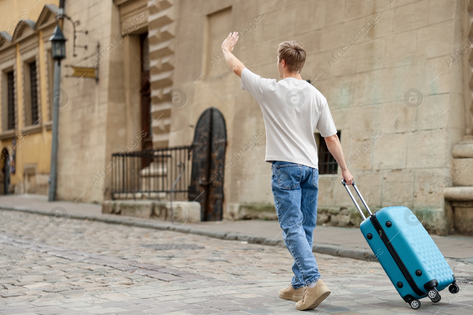 Goodbye. Man with luggage waving on city street, back view. Space for text Photo of Goodbye. Man with luggage waving on city street, back view. Space for text