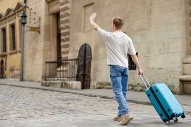 Photo of Goodbye. Man with luggage waving on city street, back view. Space for text