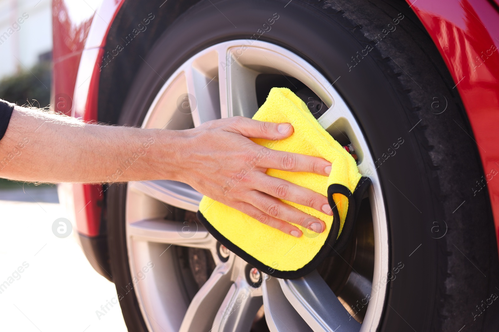 Man wiping car wheel with yellow microfiber rag outdoors, closeup Photo of Man wiping car wheel with yellow microfiber rag outdoors, closeup