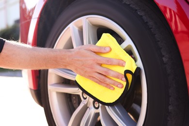 Photo of Man wiping car wheel with yellow microfiber rag outdoors, closeup