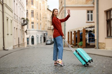 Photo of Goodbye. Woman with luggage waving on city street
