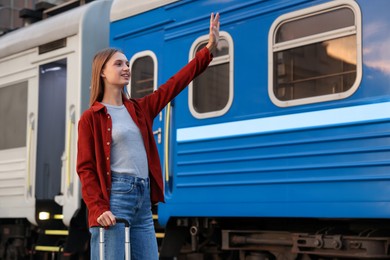 Photo of Goodbye. Happy woman with luggage waving near train outdoors, low angle view