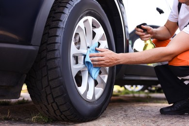 Photo of Man wiping car wheel with blue microfiber rag outdoors, closeup