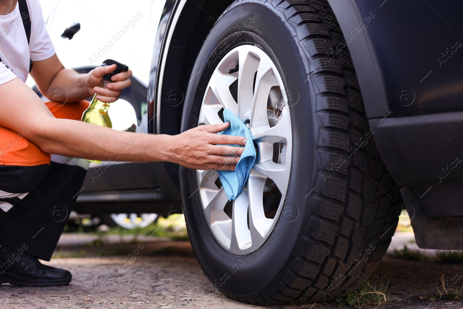 Man wiping car wheel with blue microfiber rag outdoors, closeup Photo of Man wiping car wheel with blue microfiber rag outdoors, closeup