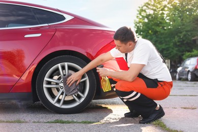 Photo of Man wiping car wheel with grey microfiber rag outdoors