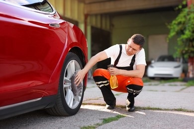 Photo of Man wiping car wheel with grey microfiber rag outdoors