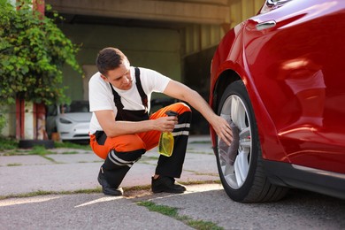 Photo of Man wiping car wheel with grey microfiber rag outdoors