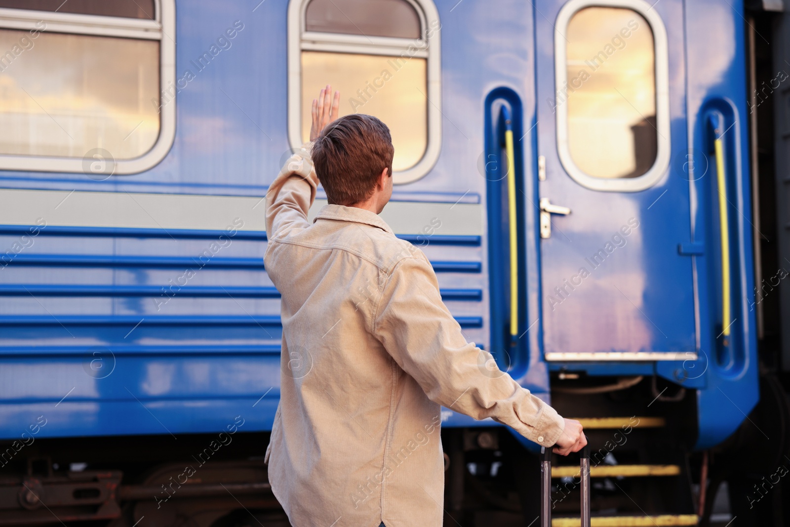 Photo of Goodbye. Man with luggage waving near train outdoors, back view