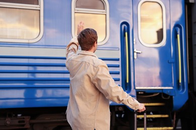 Photo of Goodbye. Man with luggage waving near train outdoors, back view