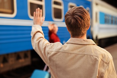 Photo of Goodbye. Man waving to his girlfriend near train outdoors, selective focus