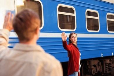 Photo of Goodbye. Man waving to his girlfriend near train outdoors, selective focus