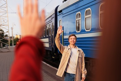 Photo of Goodbye. Woman waving to her boyfriend near train outdoors, selective focus
