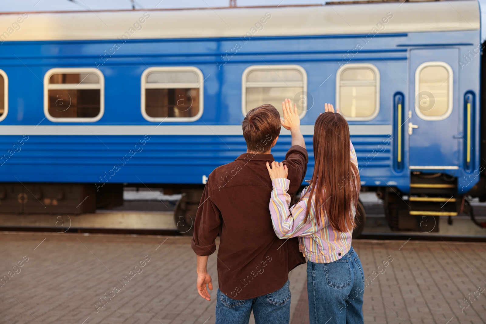 Goodbye. Couple waving on platform of railway station, back view. Space for text Photo of Goodbye. Couple waving on platform of railway station, back view. Space for text