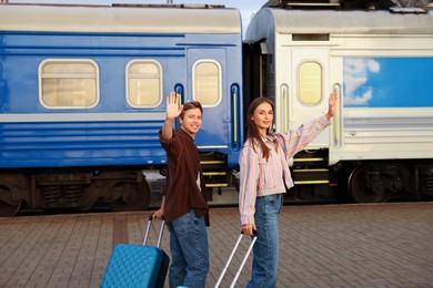 Photo of Goodbye. Couple with suitcases waving on platform of railway station