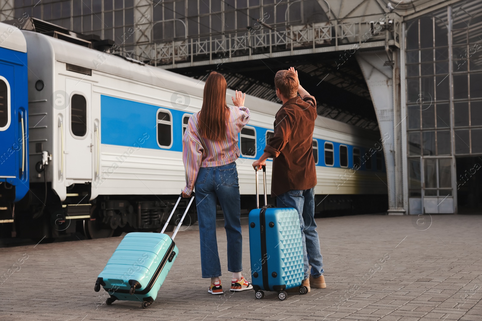 Goodbye. Couple with suitcases waving on platform of railway station, back view Photo of Goodbye. Couple with suitcases waving on platform of railway station, back view