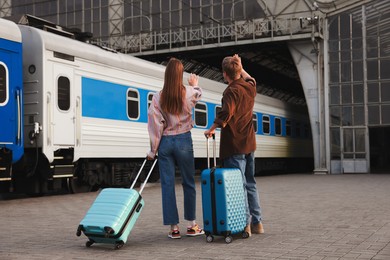 Photo of Goodbye. Couple with suitcases waving on platform of railway station, back view