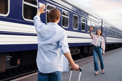 Photo of Goodbye. Man waving to his girlfriend near train outdoors, selective focus