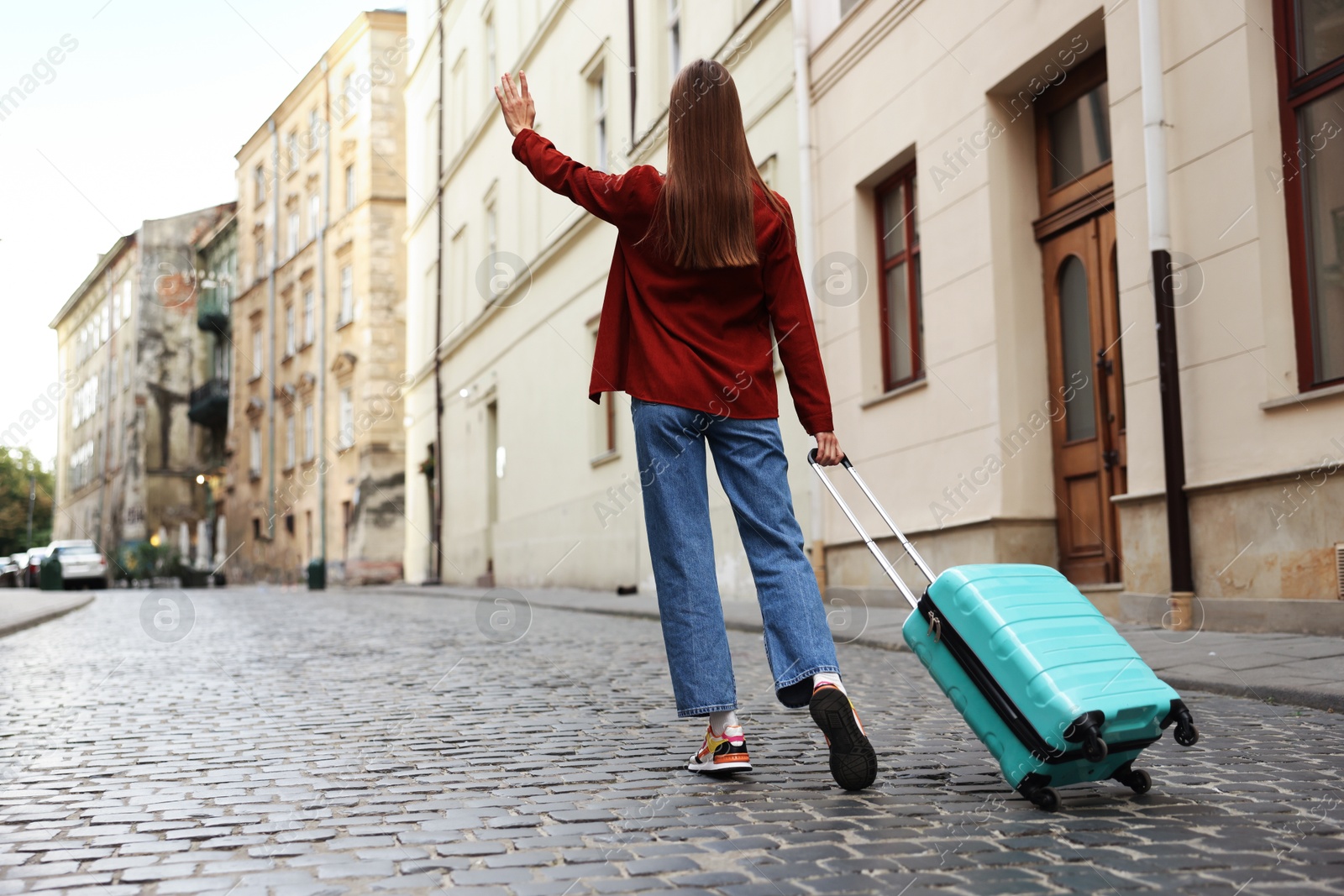 Photo of Goodbye. Woman with luggage waving on city street, back view. Space for text