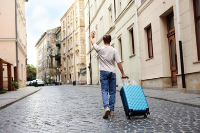 Photo of Goodbye. Man with luggage walking on city street, back view. Space for text