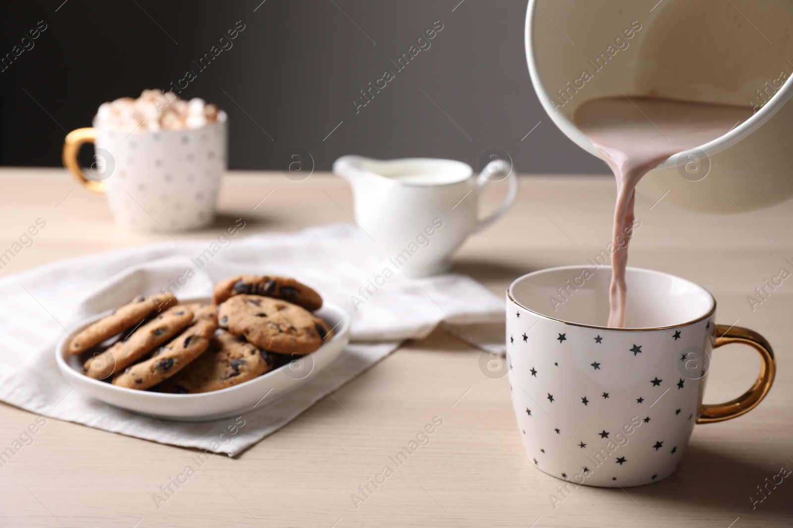 Photo of Pouring cocoa into cup near cookies on wooden table