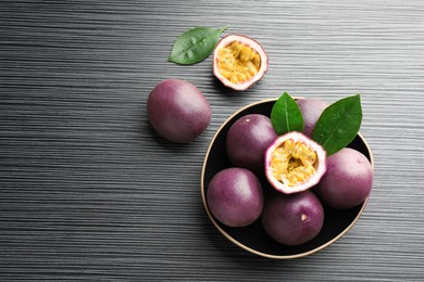Photo of Fresh passion fruits with green leaves on black wooden table, flat lay. Space for text