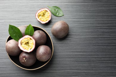 Photo of Fresh passion fruits with green leaves on black wooden table, flat lay. Space for text