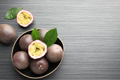 Photo of Fresh passion fruits with green leaves on black wooden table, flat lay. Space for text