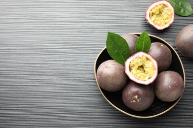 Photo of Fresh passion fruits with green leaves on black wooden table, above view. Space for text