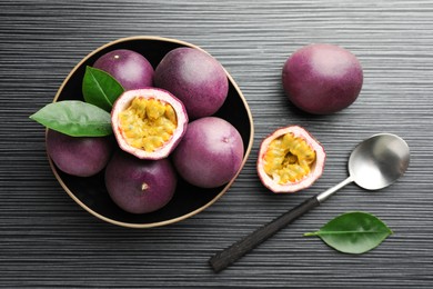 Photo of Fresh passion fruits with green leaves and spoon on black wooden table, flat lay