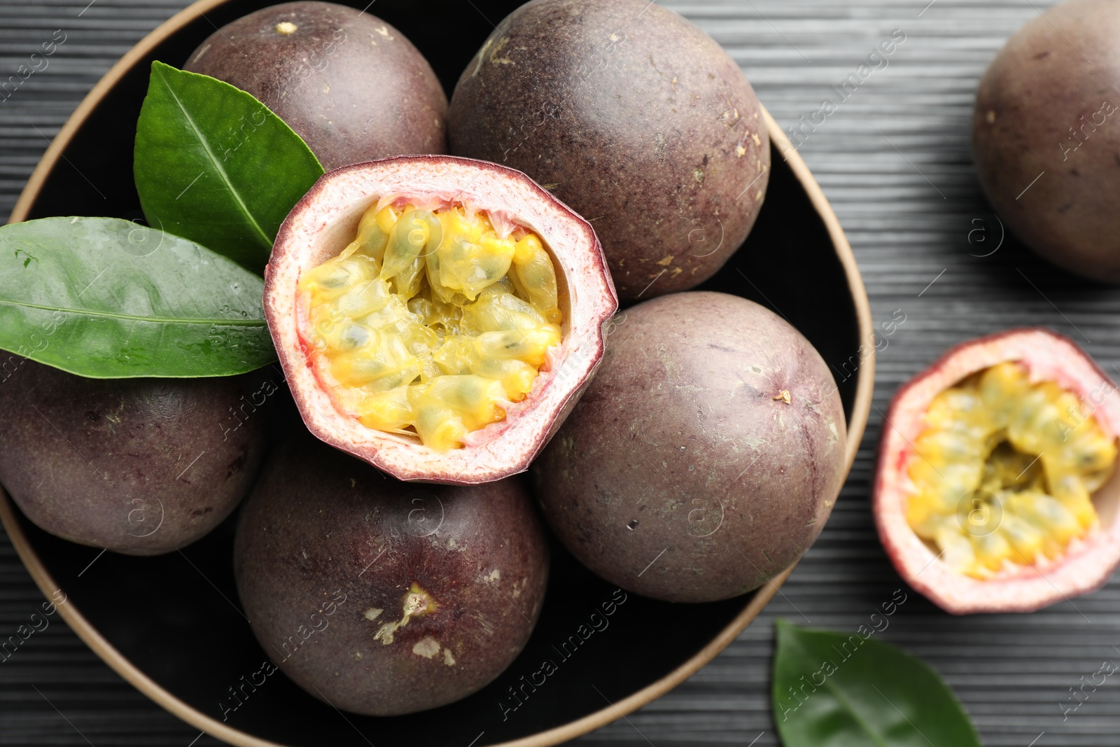 Fresh passion fruits with green leaves on black wooden table, closeup Photo of Fresh passion fruits with green leaves on black wooden table, closeup