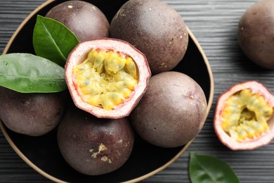Photo of Fresh passion fruits with green leaves on black wooden table, closeup