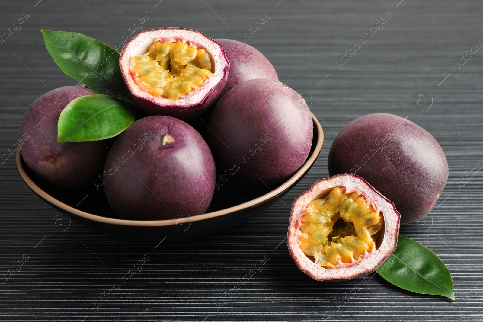 Fresh passion fruits with green leaves on black wooden table, closeup Photo of Fresh passion fruits with green leaves on black wooden table, closeup
