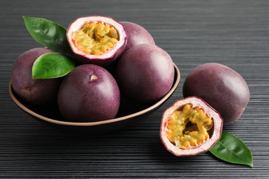 Photo of Fresh passion fruits with green leaves on black wooden table, closeup