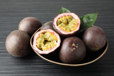 Photo of Fresh passion fruits with green leaves on black wooden table, closeup