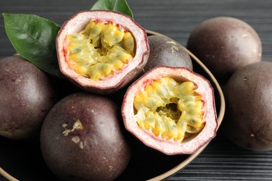 Photo of Fresh passion fruits with green leaves on black wooden table, closeup