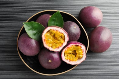 Photo of Fresh passion fruits with green leaves on black wooden table, above view