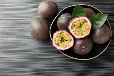 Photo of Fresh passion fruits with green leaves on black wooden table, above view. Space for text