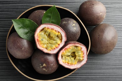Photo of Fresh passion fruits with green leaves on black wooden table