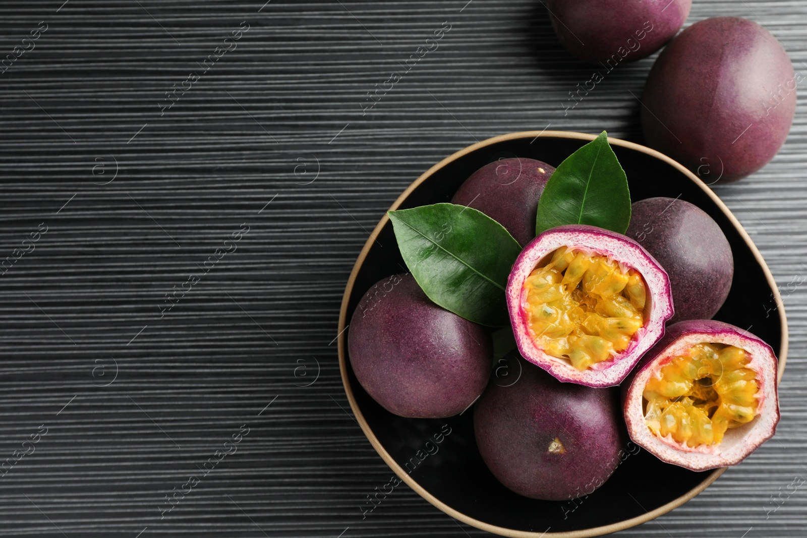 Fresh passion fruits with green leaves on black wooden table, above view. Space for text Photo of Fresh passion fruits with green leaves on black wooden table, above view. Space for text