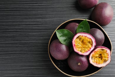Photo of Fresh passion fruits with green leaves on black wooden table, above view. Space for text
