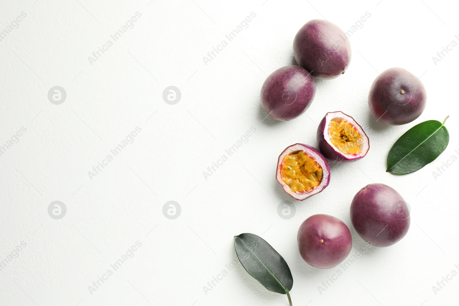 Photo of Fresh passion fruits with green leaves on white table, flat lay. Space for text