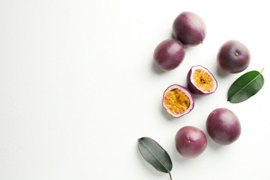 Photo of Fresh passion fruits with green leaves on white table, flat lay. Space for text