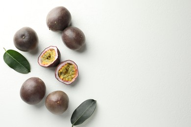 Photo of Fresh passion fruits with green leaves on white table, flat lay. Space for text